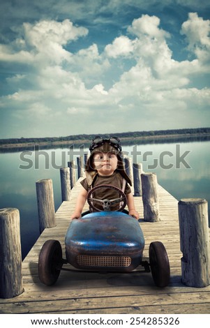 Happy little boy driving big vintage old toy car on footbridge at lake and having fun