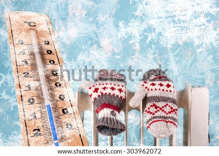 gloves on a radiator / heater with frozen thermometer on a blue cold winter background