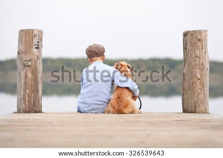 little boy sitting with his dog on the shore of Lake, child hugging his dog