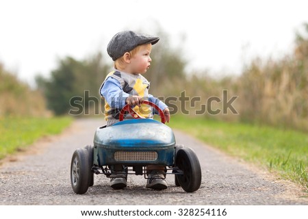 Happy little boy driving big vintage old toy car and having fun, outdoors. Kid leisure on autumn day