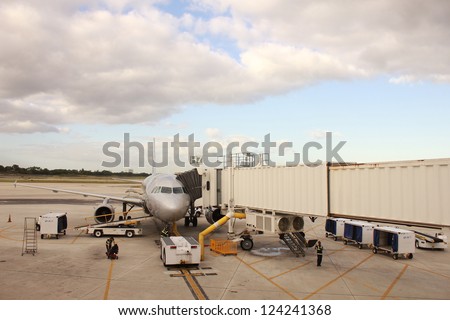 Airplane near the terminal in an airport. Trucks and ladder near airplane.