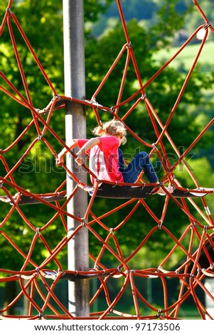 small blonde girl climbing a rope climbing frame wearing a pink T-shirt and blue jeans