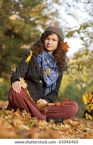 Girl sitting in autumn with falling leaves
