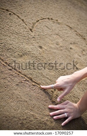 stock photo : a womans hand drawing a heart on the beach to show the love