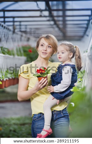 people - children, gardening and occupation concept - happy children taking care of the flowers in the greenhouse. Mom showing baby flowers and playing with your child