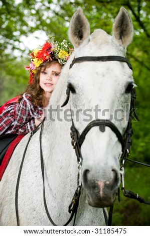 Little girl in floral wreath riding horse in the forest