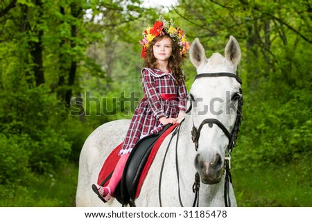 Little cute girl in floral wreath riding horse in the forest