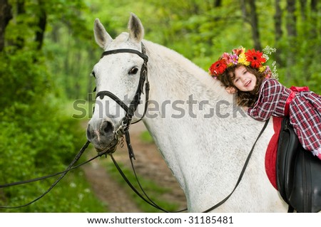 Smiling little girl in floral wreath riding horse in the forest