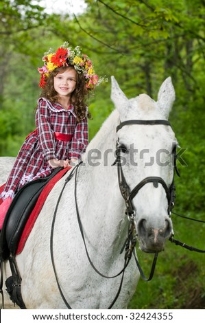 Smiling little girl in floral wreath riding horse in the forest