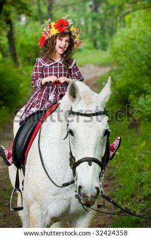 Laughing little girl in floral wreath riding horse in the forest