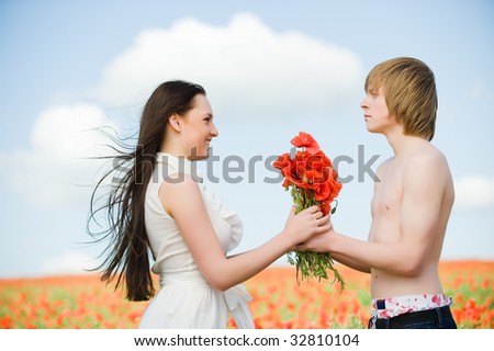 Lovely young couple in the poppy field, with bouquet of flowers
