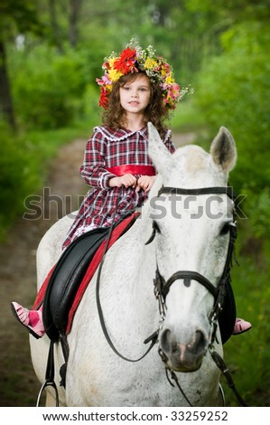 Cute little girl in floral wreath riding horse in the forest