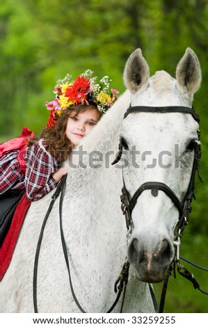 Beautiful little girl in floral wreath riding horse in the forest