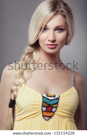 Beautiful blonde young woman with braid hairdo in yellow dress, looking at camera