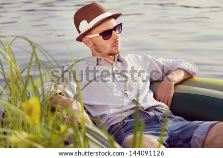 Portrait of a young handsome man resting in a boat on the lake, sunny summer day