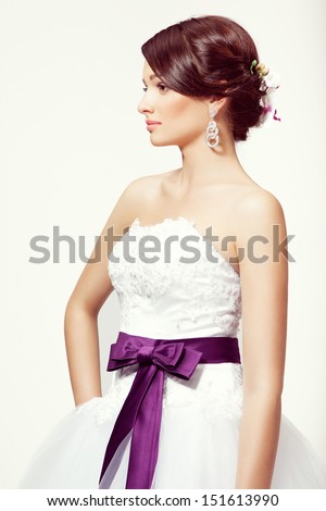 Portrait of a beautiful brunette bride with orchid in hairdo and white wedding dress, in studio