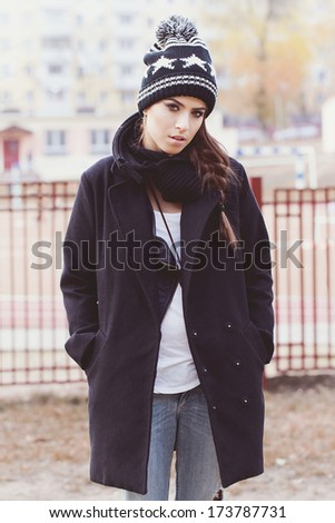 Fashionable stylish brunette girl in coat and beanie walking on the street. Looking at camera. Lifestyle. Urban city style. Outside