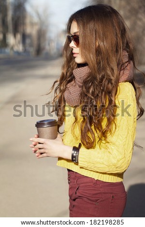 Portrait of beautiful brunette girl with takeaway drink standing on the street. Urban city scene. Warm sunny weather. Outdoors