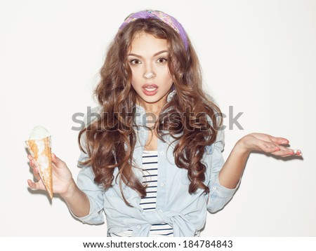 Pretty brunette girl having fun, ice cream on her nose and hands. Surprised, looking at camera. Indoors, lifestyle