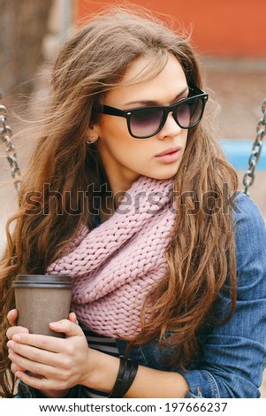 Portrait of a beautiful brunette girl in sunglasses holding drink in her hands, in park. Warm sunny day. Outdoors