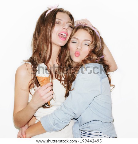 Pretty brunette girls with bright makeup and pink lips. Wearing headband. One keeping ice cream and hugging her friend. Other  sending kiss. Inside