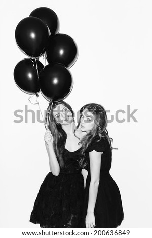 Pretty girls having fun. One keeping black balloons in her hand and smiling. Inside