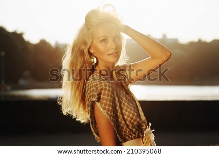 Closeup portrait of beautiful blonde girl with earrings standing in park in sunset light