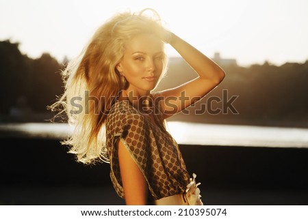 Closeup portrait of beautiful blonde girl standing in park in sunset light. Outdoors
