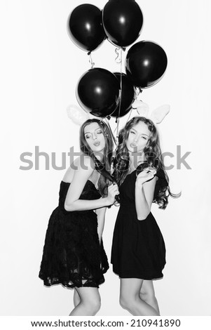 Pretty girls with bunny ears and pink lips having fun. Holding black balloons in hands. Inside
