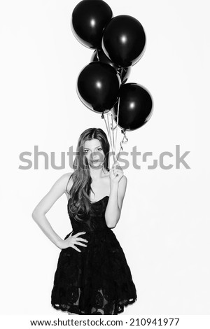 Pretty girl holding black balloons in her hand. Smiling. Wearing black dress. Inside