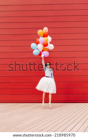 Jumping girl with colorful balloons in her hand. Outside. Red background