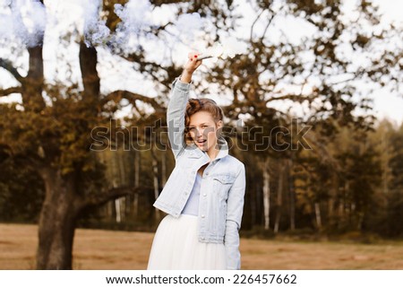 Portrait of beautiful blonde girl wearing casual clothes keeping smoke popper in her hand. Nature background. Outdoors