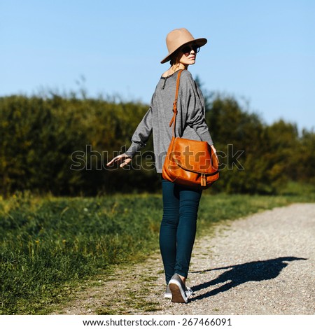 Young beautiful girl walking down country road. Warm summer evening. Nature background. Blue sky and green grass. Outdoors