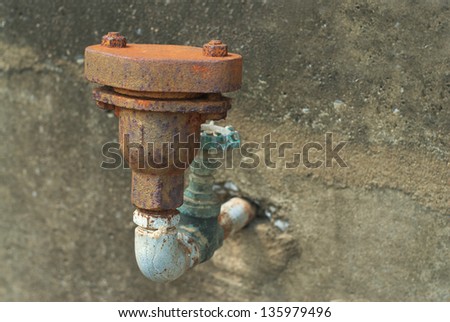 rusty metal water pipe with a valve against concrete wall