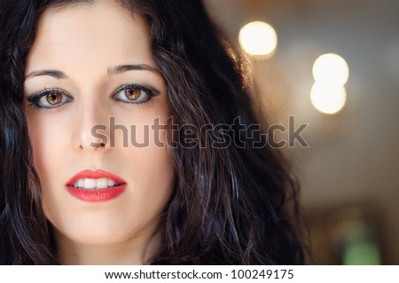 A close up of a brunette woman face, with fair, thin, smooth skin. She has brown eyes and red lips