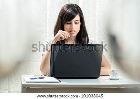 Woman working at home with a laptop while she bites the arm of her glasses.