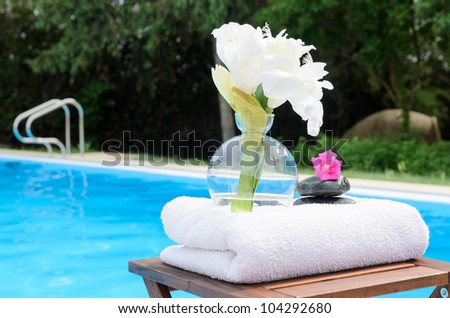 Swimming pool summer concept. Spa flower, towel and pebble. Copy space.