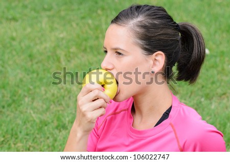 Young woman with sport wear eating and apple with green background.