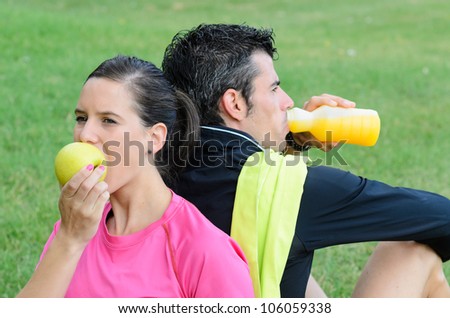 Couple of athletes, eating apple and drinking isotonic drink. Sport people after training taking a break outdoor.