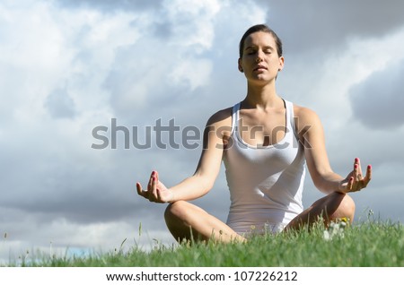Woman doing yoga on nature. Young healthy woman in lotus posture doing breathing exercise on cloudy background. Copy space.