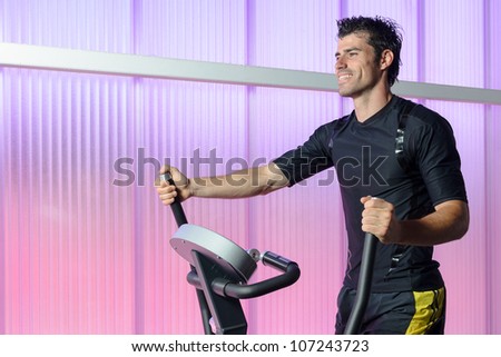 Athlete doing cardio exercise in elliptical machine. Caucasian handsome man training indoor in gym. Copy space.