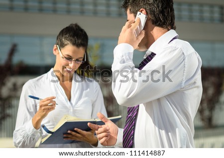 Boss dictating notes to his cheerful assistant while talking by phone.