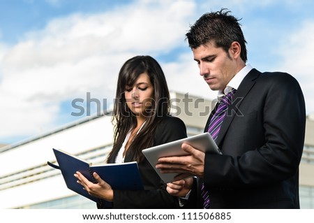Business people taking notes in front of company building. Businessman and businesswoman working together in front of corporate building.