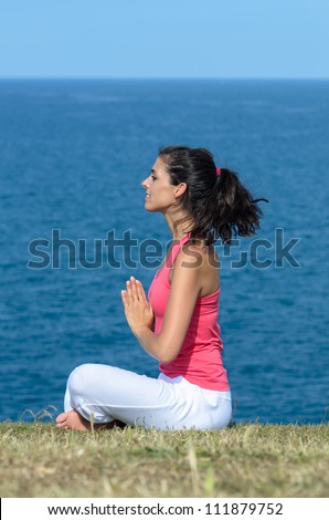 Young brunette woman doing yoga, meditation and breathing exercises  toward the sea in summer day.