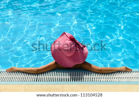 Summer woman relaxing into swimming pool leaning back on the edge. Woman with pink straw hat on hot summer holidays. Copy space.