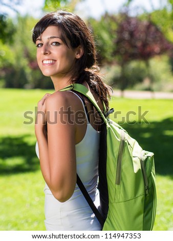 Beautiful college student with backpack  in park. Hispanic caucasian beautiful young woman on green background.