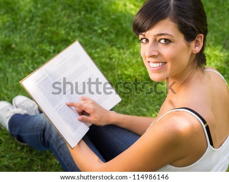 Girl student reading book outside in park. Happy caucasian hispanic college student smiling and looking at camera.