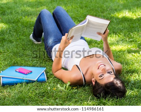 Student reading book in park. Happy caucasian girl studying outdoor in university campus. Caucasian brunette model.