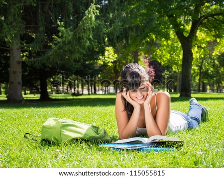 Female student reading outdoor in park. Happy caucasian college student lying down on grass on summer. Copy space.
