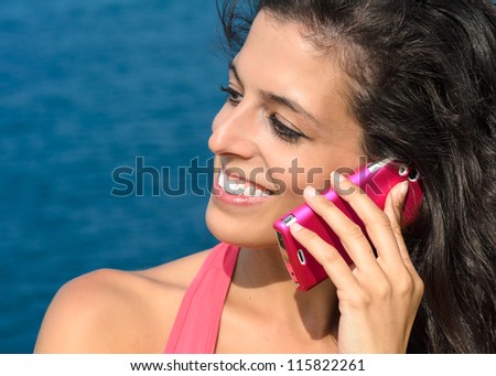 Close up of beautiful woman face talking by cell phone and smiling on blue sea background in summer. Caucasian model using mobile.